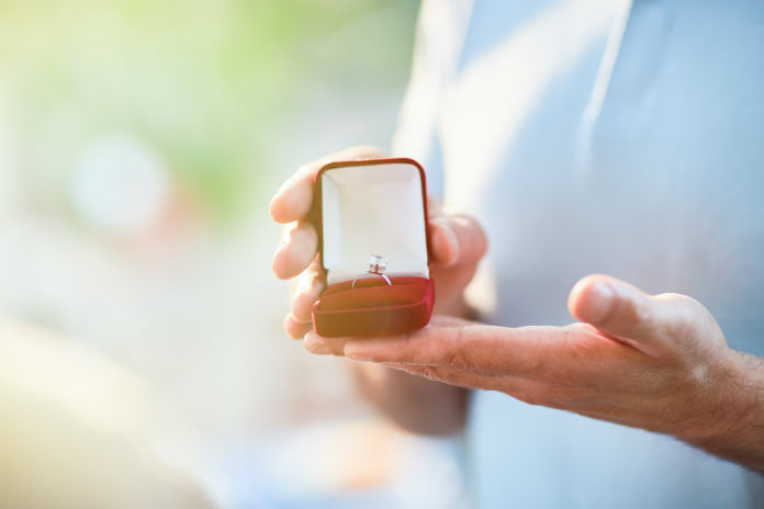 two hands presenting a ring in a box